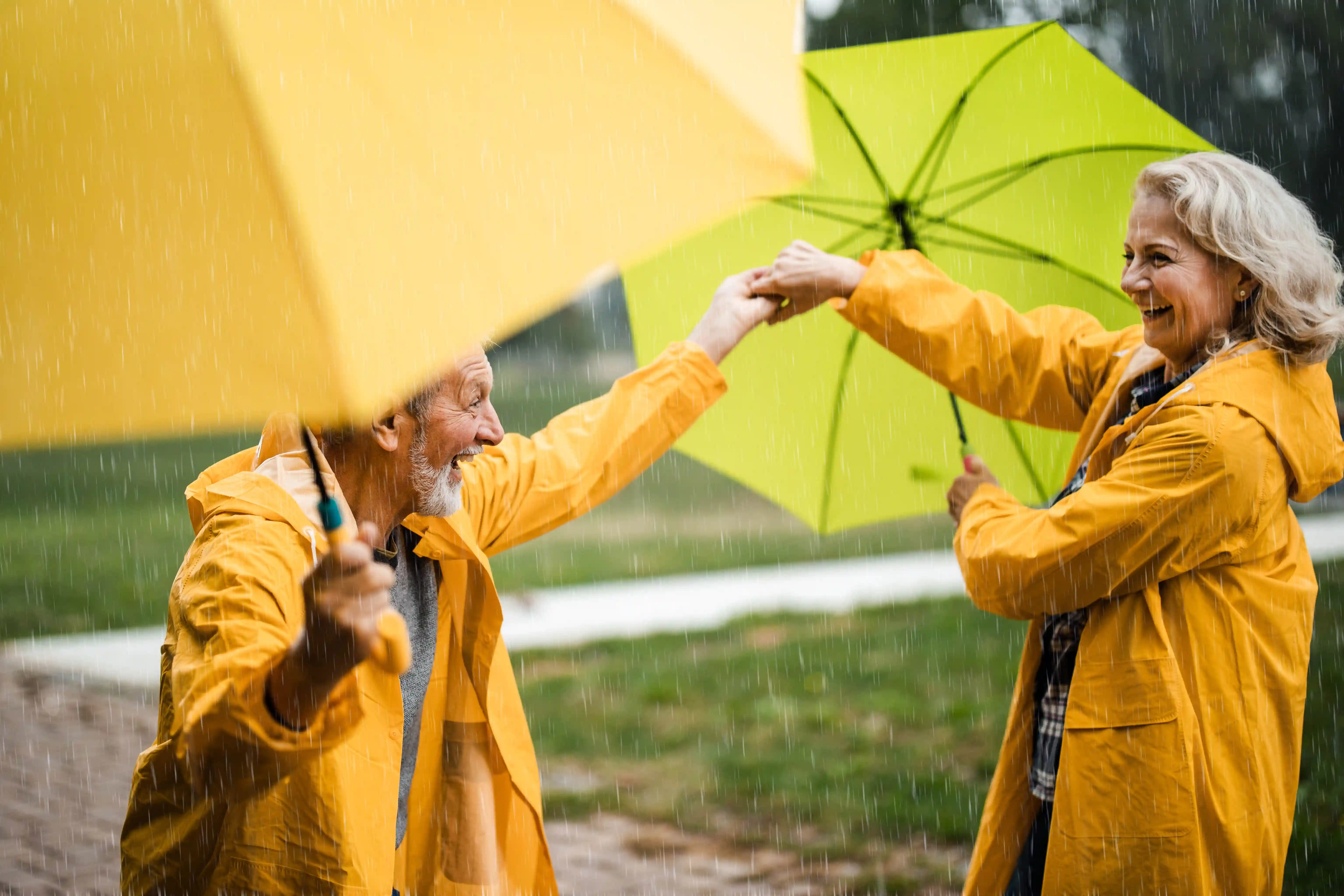 Senioren tanzen im Regen mit Regenschirm.